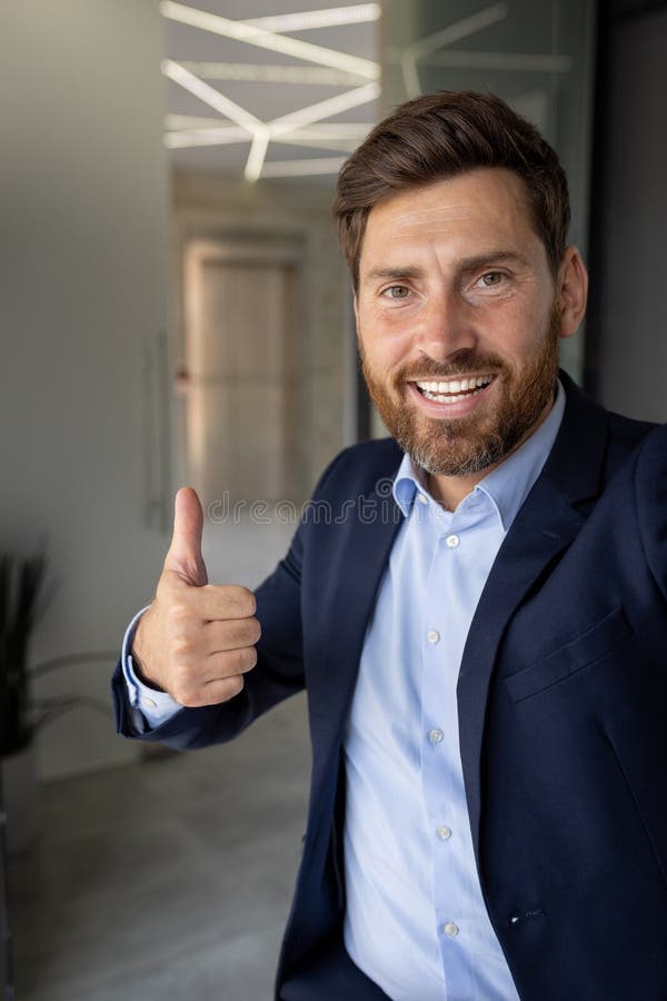 一位微笑成功的年轻男子在办公室工作并在视频通话中讲话的垂直特写照片 免版税库存照片