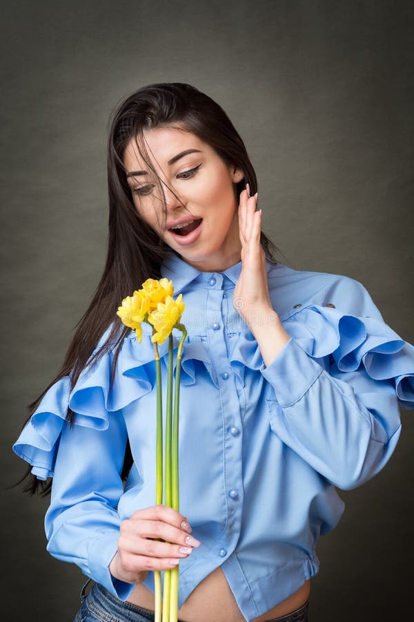 一名美丽的愉快的深色的妇女的特写镜头画象拿着黄色jonquils和微笑以欢欣的蓝色衬衣的在她的手上 免版税库存图片 一名美丽的愉快的深色的妇女的特写镜头画象拿着黄色jonquils和微笑以欢欣的蓝色衬衣的在她的手上 免版税库存图片