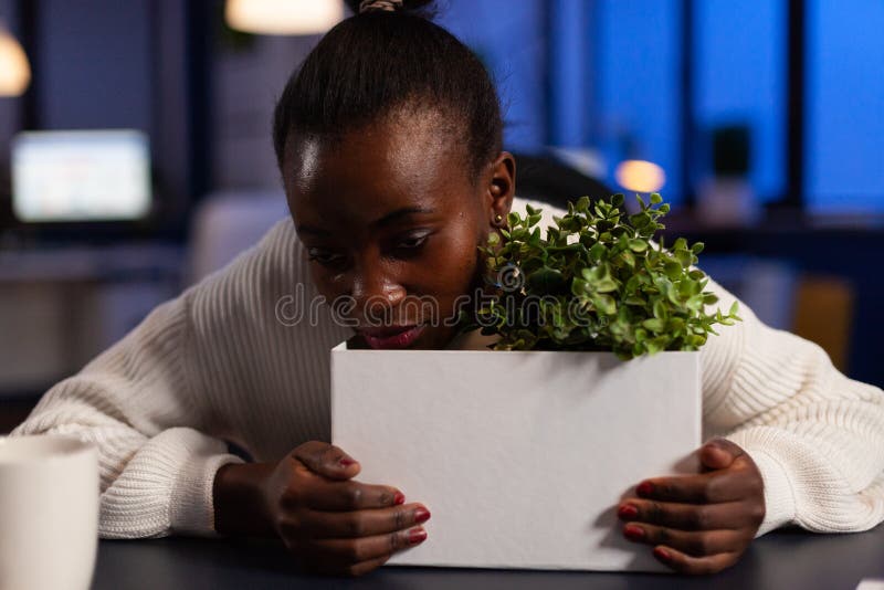 Sad dismissed african american businesswoman standing with head on cardboard box after is fired late at night in startup company office. Black entrepreneur woman having relocation situation. Sad dismissed african american businesswoman standing with head on cardboard box after is fired late at night in startup company office. Black entrepreneur woman having relocation situation