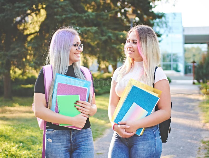 一头五颜六色的发型，站在大学校园里，拿着小册子和背包回到学校的年轻快乐的女生 库存图片