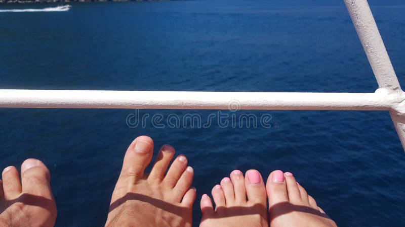 Legs of a guy and a girl, from a ship, against a background of blue, addressable sea and boat. Legs of a guy and a girl, from a ship, against a background of blue, addressable sea and boat