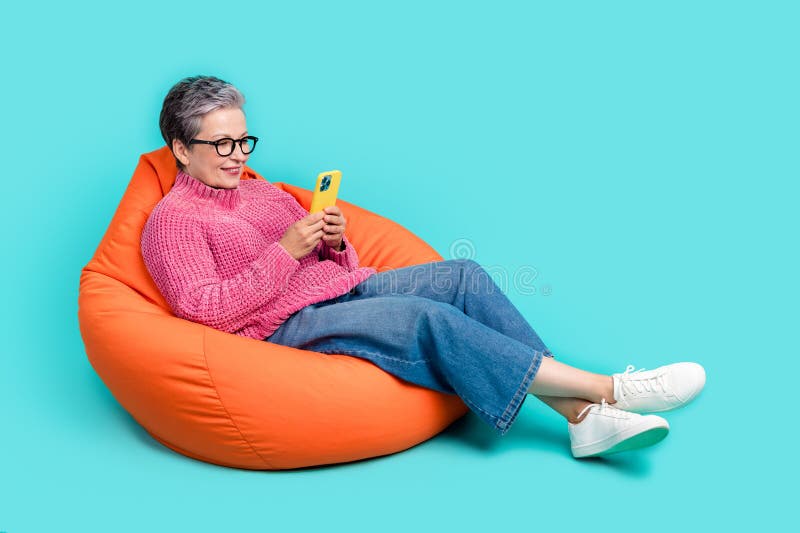 Full length photo of clever woman wear pink sweater denim pants lay on bean bag read email on smartphone isolated on teal color background. Full length photo of clever woman wear pink sweater denim pants lay on bean bag read email on smartphone isolated on teal color background.