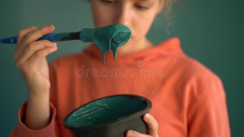 一把刷子和一碗蓝色油漆的特写,与一个穿橙色运动衫的少女的肖像对比. 肖像 股票视频