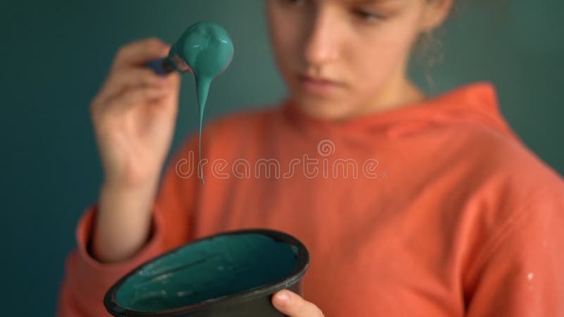 一把刷子和一碗蓝色油漆的特写,与一个穿橙色运动衫的少女的肖像对比. 肖像 股票录像