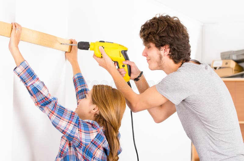 Couple renovating together as men using power drill on wood part and women helping out by holding. Couple renovating together as men using power drill on wood part and women helping out by holding.