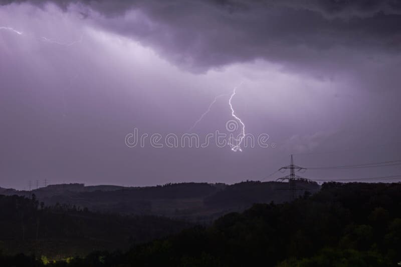 A powerful electric discharge of purple lightning strikes a power line across a vast open field. A powerful electric discharge of purple lightning strikes a power line across a vast open field