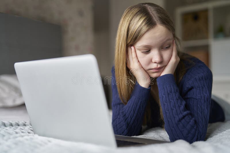 Unhappy Teenage Girl With Laptop Lying On Bed At Home Anxious About Social Media Online Bullying And Being Online Too Much. Unhappy Teenage Girl With Laptop Lying On Bed At Home Anxious About Social Media Online Bullying And Being Online Too Much