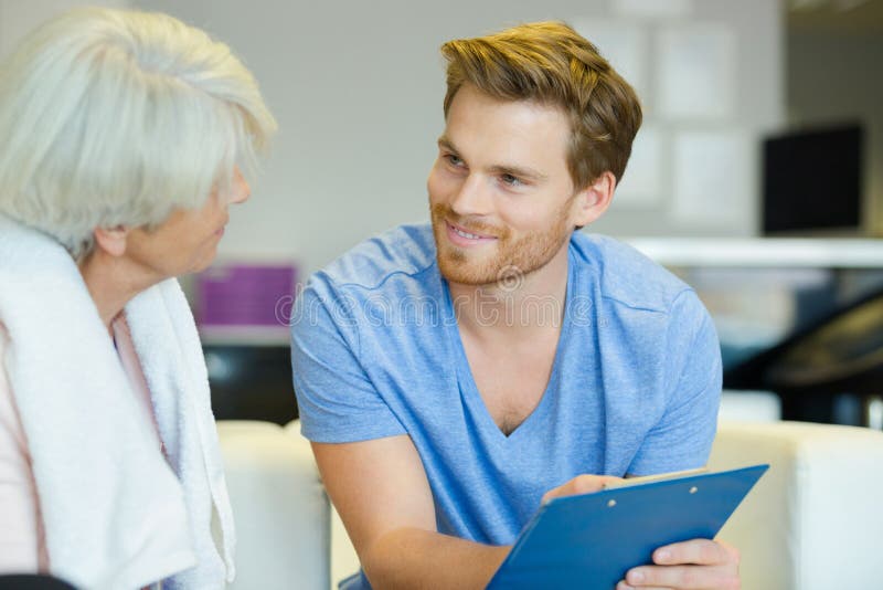 微笑的男性教练在健身房里拿着剪贴板和一位老年人 图库摄影