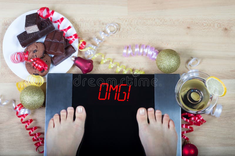 与妇女脚的数字式标度在他们和标志标志` OMG! 圣诞节装饰和不健康的食物围拢的` 免版税库存图片