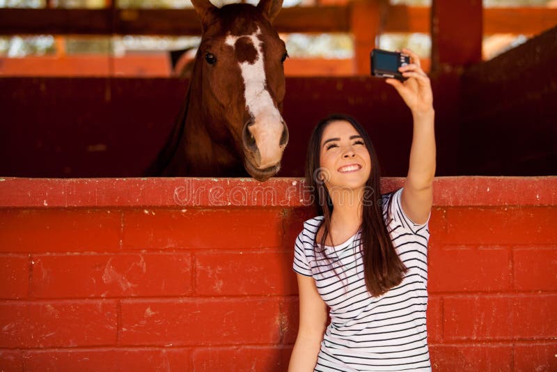 Cute young brunette taking a selfie with his horse in the stables. Cute young brunette taking a selfie with his horse in the stables