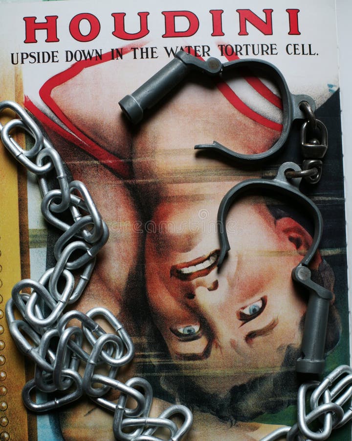 High security handcuffs as used by the police in UK with chain and Harry Houdini poster. Houdini is upside down in the water torture cell. High security handcuffs as used by the police in UK with chain and Harry Houdini poster. Houdini is upside down in the water torture cell.