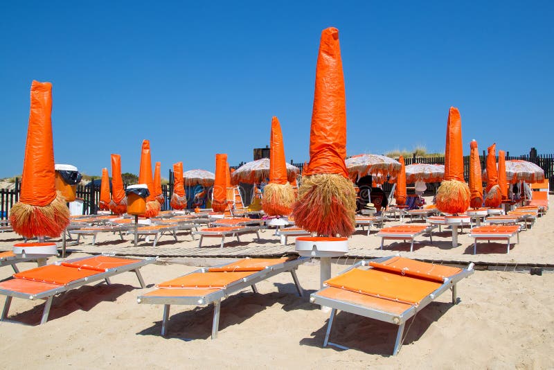 Morning empty beach with beautiful bright orange sun loungers and closed umbrellas from the sun. Yellow beach sand, bright blue sky. A beach without people. Vacation at sea. Relax day. Morning empty beach with beautiful bright orange sun loungers and closed umbrellas from the sun. Yellow beach sand, bright blue sky. A beach without people. Vacation at sea. Relax day.