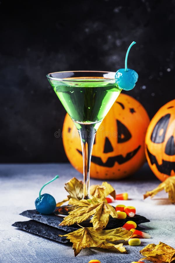 Halloween composition with festive drink, green cocktail and pumpkins lanterns and fallen leaves on night dark blue background, selective focus. Halloween composition with festive drink, green cocktail and pumpkins lanterns and fallen leaves on night dark blue background, selective focus