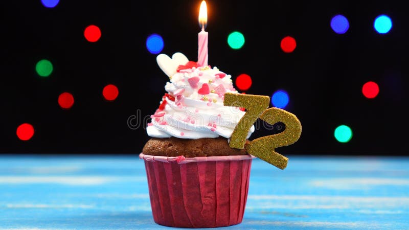与燃烧的蜡烛和第72的可口生日杯形蛋糕在多彩多姿的被弄脏的光背景