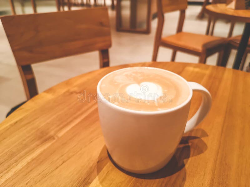 与白色心脏杯子的一白色杯子热的capuccino在棕色木桌上的上面在coffeeshop前台酒吧 免版税库存照片 与白色心脏杯子的一白色杯子热的capuccino在棕色木桌上的上面在coffeeshop前台酒吧 免版税库存照片