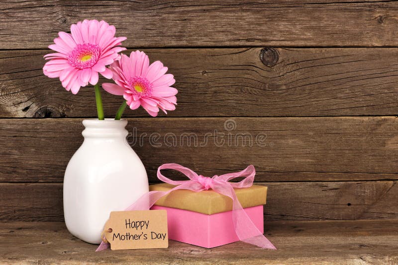 Happy Mothers Day tag with gift box and vase of pink flowers against a rustic wood background. Happy Mothers Day tag with gift box and vase of pink flowers against a rustic wood background