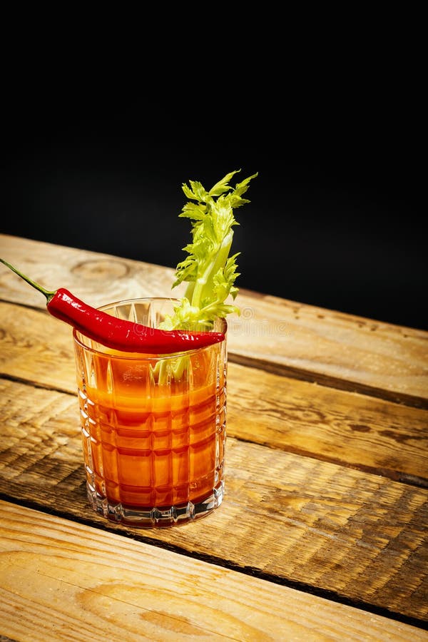 Juicy red drink bloody mary with a piece of green celery and chilli peppers on a wooden table. Juicy red drink bloody mary with a piece of green celery and chilli peppers on a wooden table