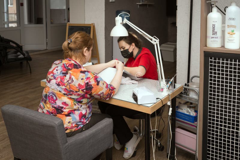 Sharypovo, Krasnoyarsk Region, RF - March 2, 2019: A professional nail technician makes  a manicure for a client at a work table in a hair and nail salon. Sharypovo, Krasnoyarsk Region, RF - March 2, 2019: A professional nail technician makes  a manicure for a client at a work table in a hair and nail salon.