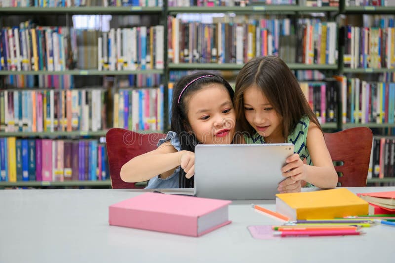 两个可爱的小女孩在学校图书馆的平板电脑上玩 无线教育和自学 免版税库存图片 两个可爱的小女孩在学校图书馆的平板电脑上玩 无线教育和自学 免版税库存图片