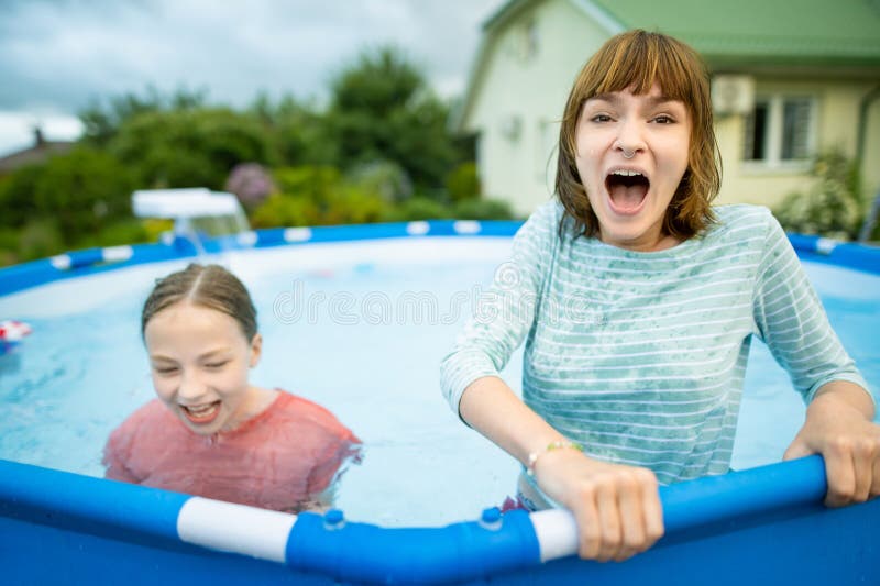 Two funny teenage sisters trying to get into cold pool water. Children having fun in outdoor pool. Family fun in a pool. Summer activities for the family with kids. Two funny teenage sisters trying to get into cold pool water. Children having fun in outdoor pool. Family fun in a pool. Summer activities for the family with kids