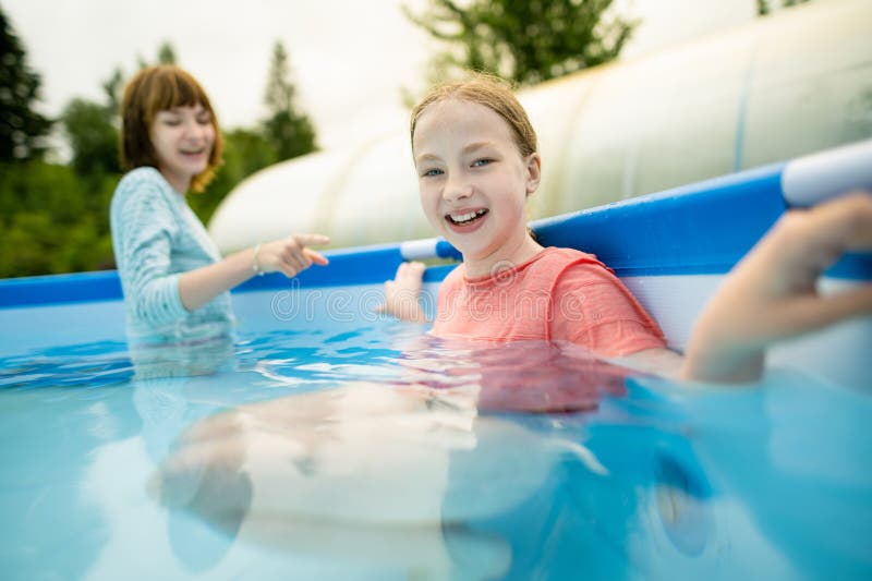 Two funny teenage sisters trying to get into cold pool water. Children having fun in outdoor pool. Family fun in a pool. Summer activities for the family with kids. Two funny teenage sisters trying to get into cold pool water. Children having fun in outdoor pool. Family fun in a pool. Summer activities for the family with kids