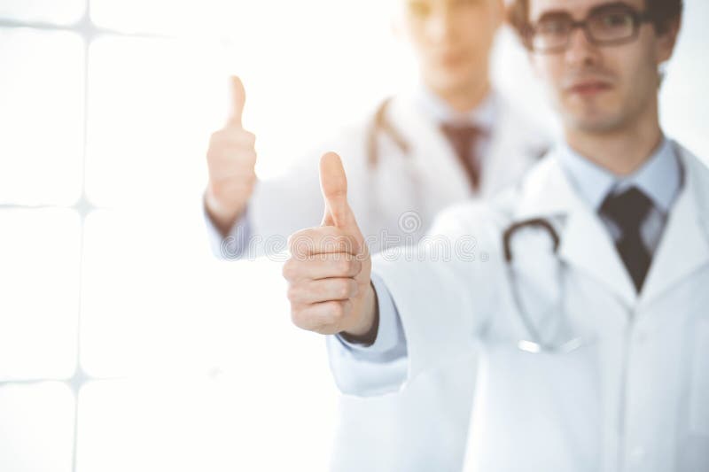 两位男医生站在一起，竖起大拇指，象征着在阳光明媚的诊所为病人提供最佳服务 免版税库存照片