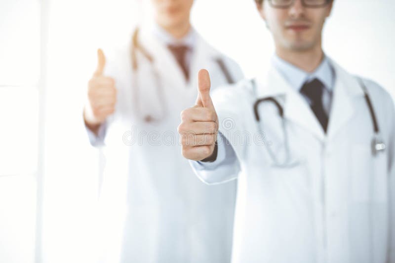 两位男医生站在一起，竖起大拇指，象征着在阳光明媚的诊所为病人提供最佳服务 库存图片