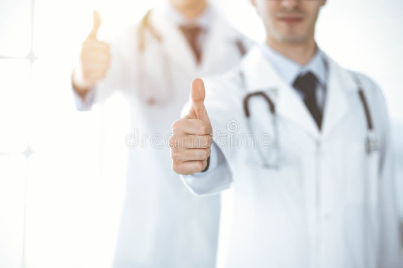 两位男医生站在一起，竖起大拇指，象征着在阳光明媚的诊所为病人提供最佳服务 免版税图库摄影