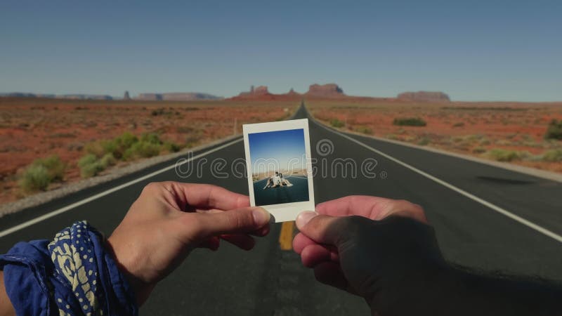 两只手握着一张与一对夫妇在亚利桑那州沙漠公路上的迷人瞬间照片的电影特写.