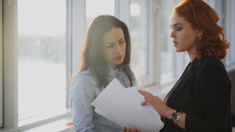 两名年轻美丽的妇女在窗口附近谈论不同的文件