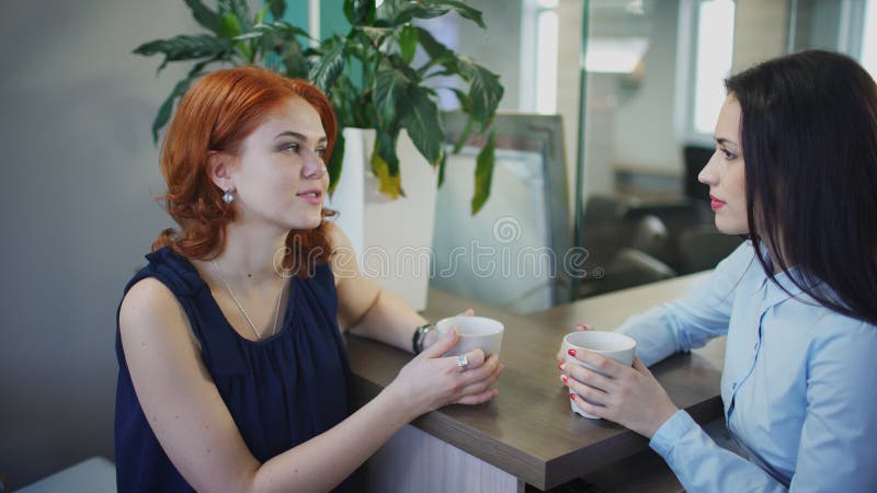 两名年轻美丽的妇女谈话在咖啡在办公室