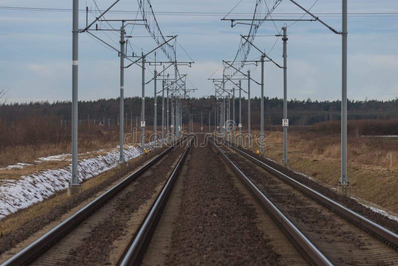 A view of the two-track, electrified railway track.
Winter, cloudy day. The ground is covered with sheets of snow. A two-track, electrified railway track. You can see the elements of electric traction in the form of metal poles, electric cables. Straight rails leading to the horizon. On the embankment you can see patches of a thin layer of snow. There are fields and meadows on both sides of the tracks. A view of the two-track, electrified railway track.
Winter, cloudy day. The ground is covered with sheets of snow. A two-track, electrified railway track. You can see the elements of electric traction in the form of metal poles, electric cables. Straight rails leading to the horizon. On the embankment you can see patches of a thin layer of snow. There are fields and meadows on both sides of the tracks.