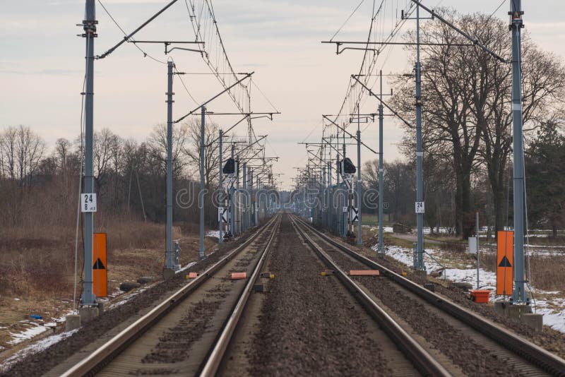 A view of the two-track, electrified railway track.
Winter, cloudy day. The ground is covered with sheets of snow. A two-track, electrified railway track. You can see the elements of electric traction in the form of metal poles, electric cables. Straight rails leading to the horizon. On the embankment you can see patches of a thin layer of snow. There are fields and meadows on both sides of the tracks. A view of the two-track, electrified railway track.
Winter, cloudy day. The ground is covered with sheets of snow. A two-track, electrified railway track. You can see the elements of electric traction in the form of metal poles, electric cables. Straight rails leading to the horizon. On the embankment you can see patches of a thin layer of snow. There are fields and meadows on both sides of the tracks.