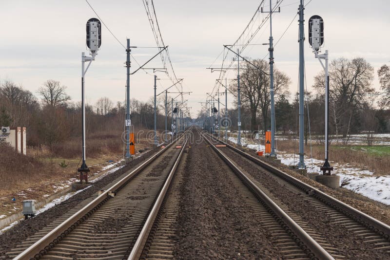 A view of the two-track, electrified railway track.
Winter, cloudy day. The ground is covered with sheets of snow. A two-track, electrified railway track. You can see the elements of electric traction in the form of metal poles, electric cables. Straight rails leading to the horizon. On the embankment you can see patches of a thin layer of snow. There are fields and meadows on both sides of the tracks. A view of the two-track, electrified railway track.
Winter, cloudy day. The ground is covered with sheets of snow. A two-track, electrified railway track. You can see the elements of electric traction in the form of metal poles, electric cables. Straight rails leading to the horizon. On the embankment you can see patches of a thin layer of snow. There are fields and meadows on both sides of the tracks.