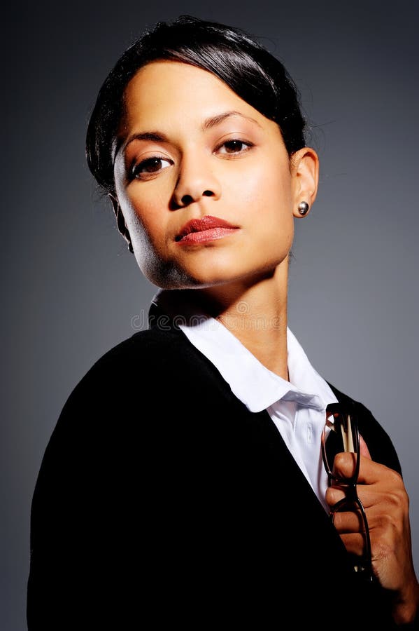 Domineering woman in business suit holding to a pair of glasses, with dramatic lighting. Domineering woman in business suit holding to a pair of glasses, with dramatic lighting