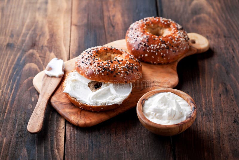 Whole grain bagels with cream cheese on wooden board, selective focus. Whole grain bagels with cream cheese on wooden board, selective focus