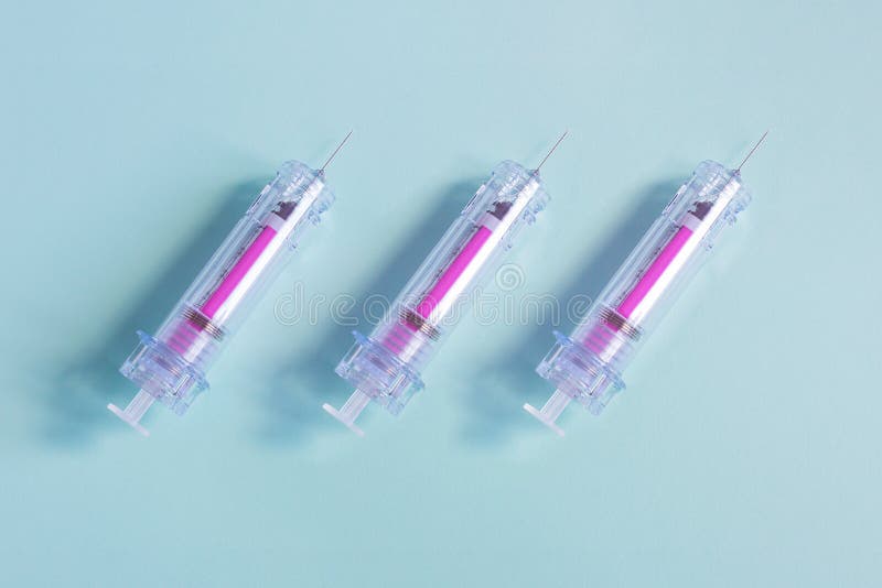 Three large vaccination syringes together with the needle uncapped forming a pattern of lines on a textured blue paper background. Health sciences and hospital medical clinical material. Three large vaccination syringes together with the needle uncapped forming a pattern of lines on a textured blue paper background. Health sciences and hospital medical clinical material