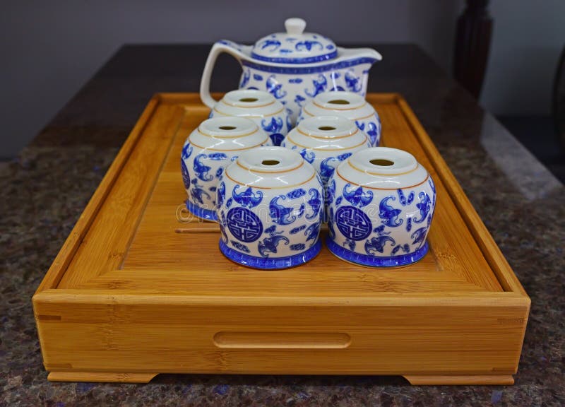Chinese blue porcelain teapot set on traditional wooden tray. The set includes a teapot with handle and six small cups with bat like motif. The tray is a practical tool where it provides support and at the same time, drinkers can wash the tea set on it and the tray below will hold the water from the washing. Chinese blue porcelain teapot set on traditional wooden tray. The set includes a teapot with handle and six small cups with bat like motif. The tray is a practical tool where it provides support and at the same time, drinkers can wash the tea set on it and the tray below will hold the water from the washing.