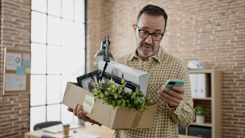 Middle age man business worker dismissed holding cardboard box using smartphone at office. Middle age man business worker dismissed holding cardboard box using smartphone at office