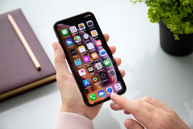 Alushta, Russia - September 24, 2018: Woman hand holding iPhone X with home screen IOS. iPhone 10 was created and developed by the Apple inc. Alushta, Russia - September 24, 2018: Woman hand holding iPhone X with home screen IOS. iPhone 10 was created and developed by the Apple inc.