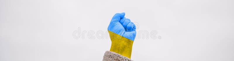 International political relationship between Ukraine and Russia. female hand fist painted in Ukraine flag colors yellow-blue against blue sky. International political relationship between Ukraine and Russia. female hand fist painted in Ukraine flag colors yellow-blue against blue sky
