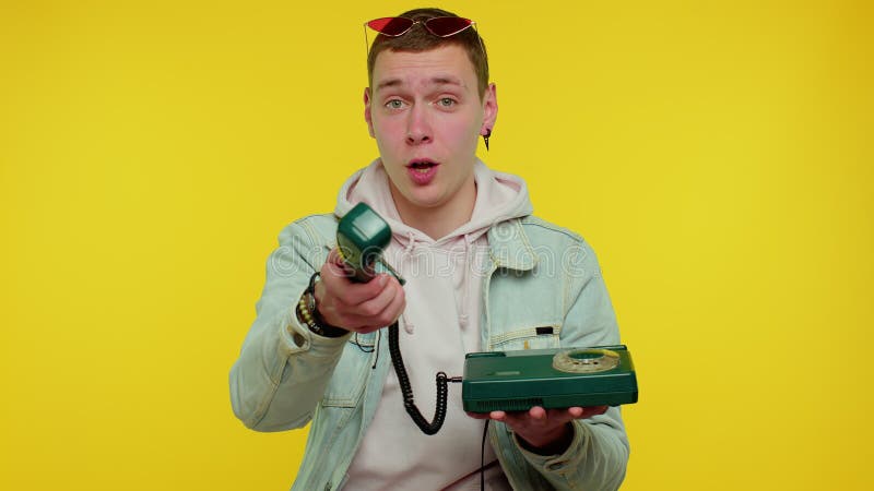 Hey you, call me back. Cheerful teen boy secretary in denim jacket talking on wired vintage telephone of 80s, says hey you call me back. Young man posing isolated on yellow studio wall background. Hey you, call me back. Cheerful teen boy secretary in denim jacket talking on wired vintage telephone of 80s, says hey you call me back. Young man posing isolated on yellow studio wall background