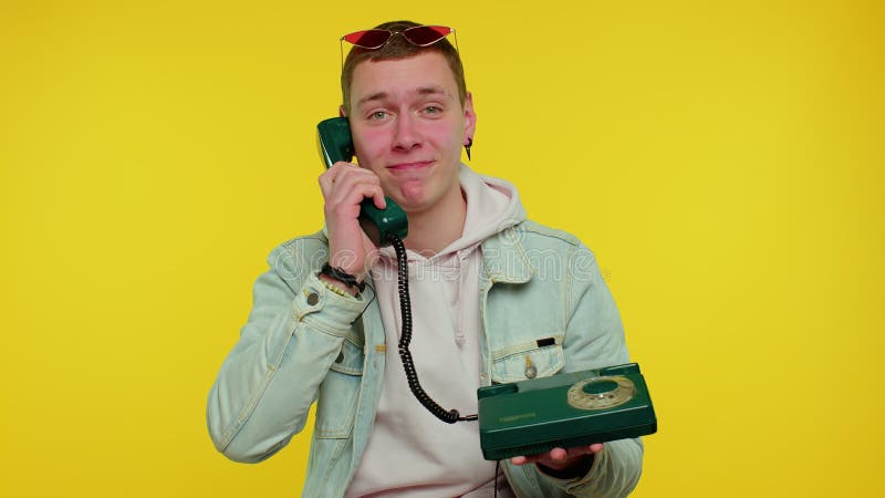 Cheerful teen boy secretary in denim jacket talking on wired vintage telephone of 80s, says hey you call me back. Hey you, call me back. Young man posing isolated on yellow studio wall background. Cheerful teen boy secretary in denim jacket talking on wired vintage telephone of 80s, says hey you call me back. Hey you, call me back. Young man posing isolated on yellow studio wall background