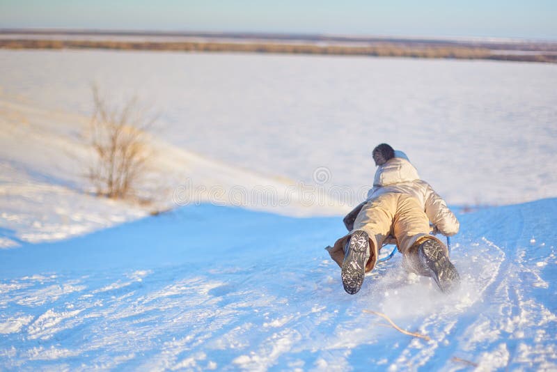 乘坐雪撬的快乐的女孩下坡在一个白色晴朗的冬天山风景的一串积雪的爬犁足迹 图库摄影 乘坐雪撬的快乐的女孩下坡在一个白色晴朗的冬天山风景的一串积雪的爬犁足迹 图库摄影