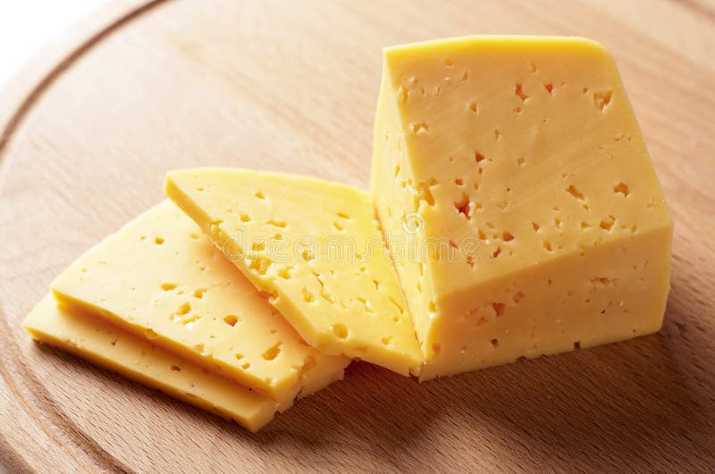 Block of cheese cut into slices or portions on a wooden cheeseboard ready to be served as an appetizer or snack, or used as a cooking ingredient. Block of cheese cut into slices or portions on a wooden cheeseboard ready to be served as an appetizer or snack, or used as a cooking ingredient