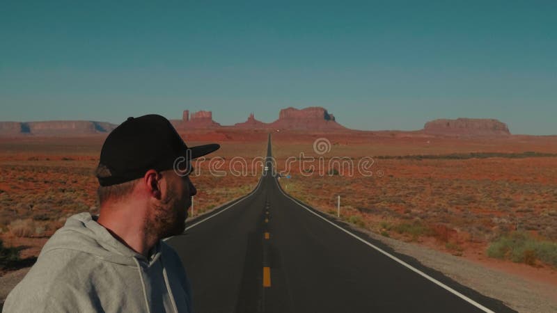 亚利桑那州阳光的砂岩沙漠中，站在高速公路中间的年轻成年男子的特写.