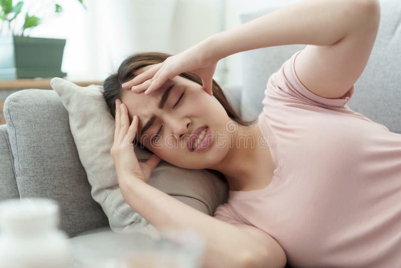 亚洲女人正用双手抱头,痛苦地睡在家的沙发上,年轻女人因此头痛 免版税库存照片 亚洲女人正用双手抱头,痛苦地睡在家的沙发上,年轻女人因此头痛 免版税库存照片