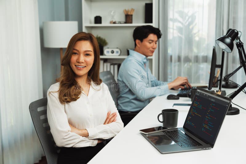 Profile smiling beautiful Asian businesswoman looking camera to portrait pose at modern office on working desk casual day. Blurry background man colleague analyzing data market plan on pc. Infobahn. Profile smiling beautiful Asian businesswoman looking camera to portrait pose at modern office on working desk casual day. Blurry background man colleague analyzing data market plan on pc. Infobahn.