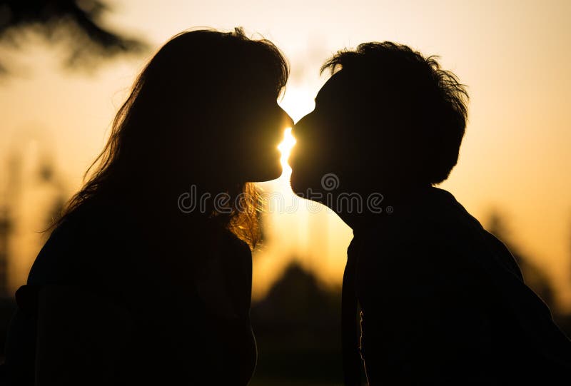 Sensual portrait of the profile in silhouette of a romantic couple kissing at sunset with sun flare between their lips. Sensual portrait of the profile in silhouette of a romantic couple kissing at sunset with sun flare between their lips