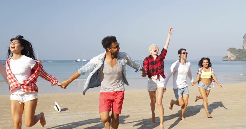 人们在度假编组在拿着手愉快的快乐的人和妇女游人的海滩三夫妇的赛跑